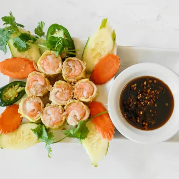 Vietnamese shrimp dumplings with fresh cilantro, sliced cucumbers, carrots, jalapeños, and a side of dipping sauce.