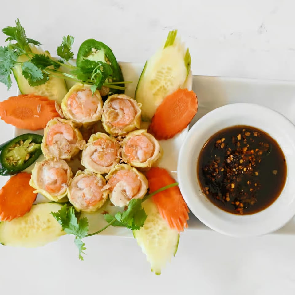 Vietnamese shrimp dumplings with fresh cilantro, sliced cucumbers, carrots, and jalapeños, served with a dark dipping sauce.