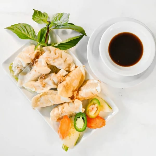 A plate of golden-brown fried Vietnamese dumplings with basil, vegetables, and a side of dipping sauce.