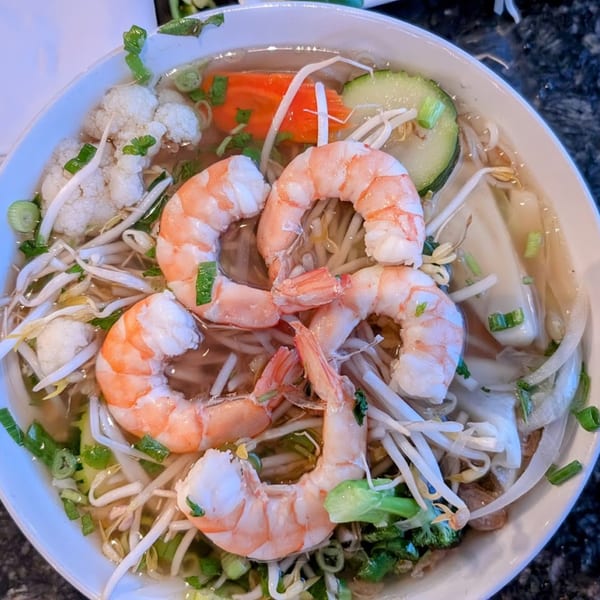 A close-up of a bowl of Vietnamese pho with shrimp, bean sprouts, and vegetables.