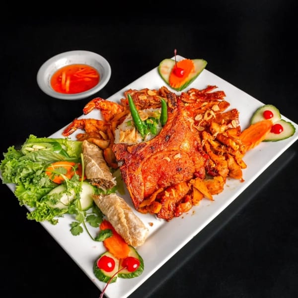 A Vietnamese platter with grilled pork chop, shrimp, spring rolls, rice, and fresh vegetables with dipping sauce.