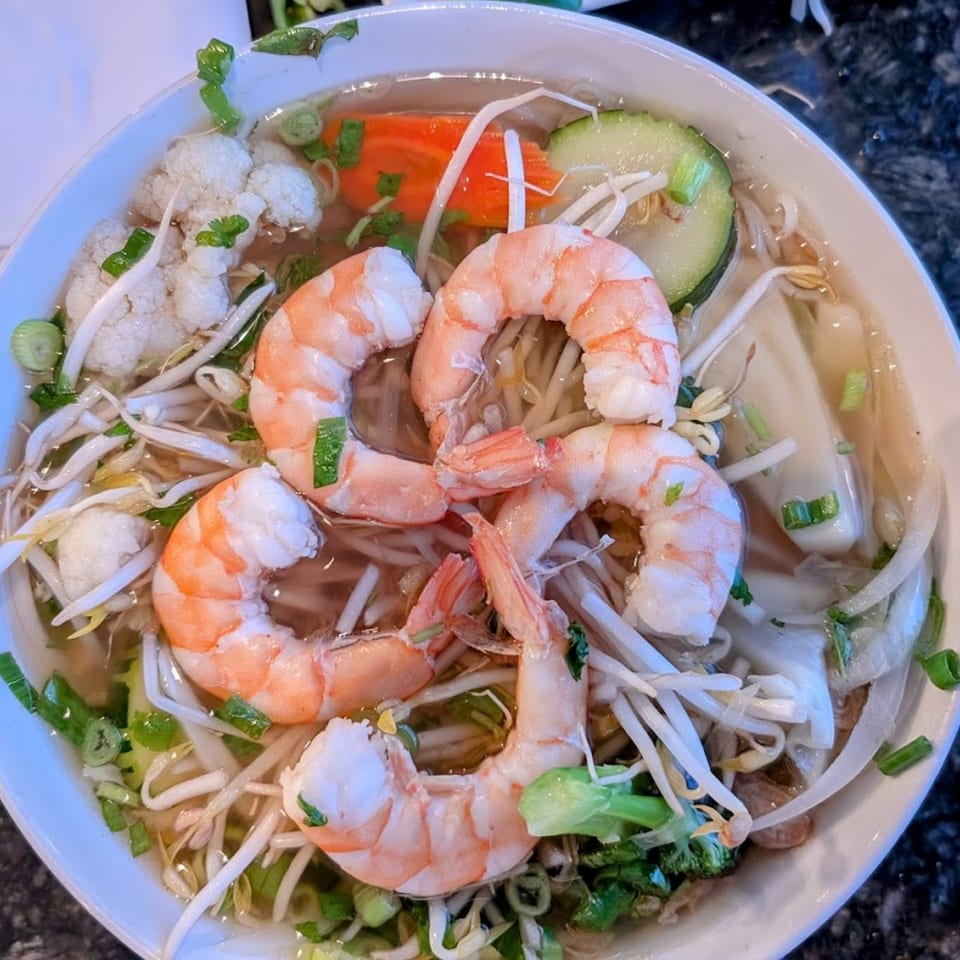 Close-up of a bowl of Vietnamese pho with shrimp, bean sprouts, and vegetables.