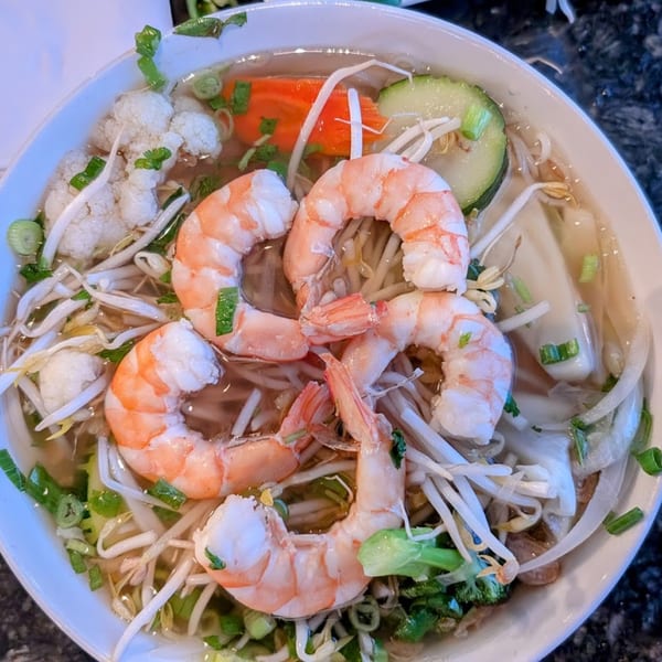 A close-up of a bowl of Vietnamese pho with shrimp, bean sprouts, and vegetables.