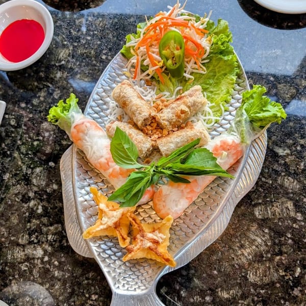 Vietnamese spring rolls, egg rolls, and wontons on a fish-shaped platter with a side of red sauce.