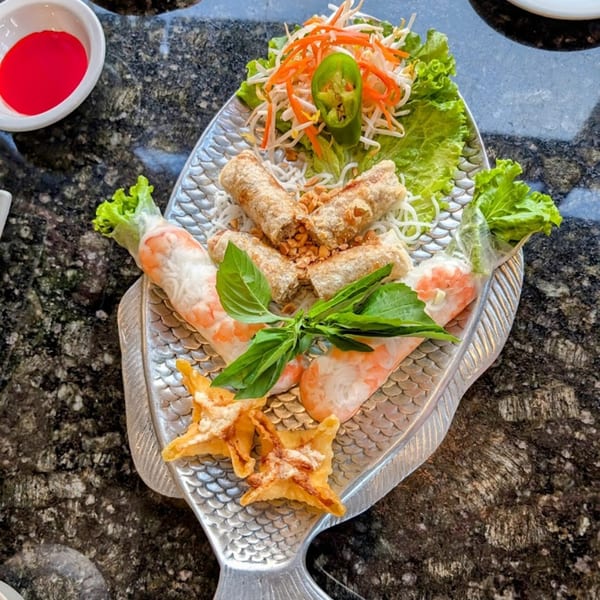 Vietnamese spring rolls, egg rolls, and wontons on a fish-shaped platter with a side of red sauce.