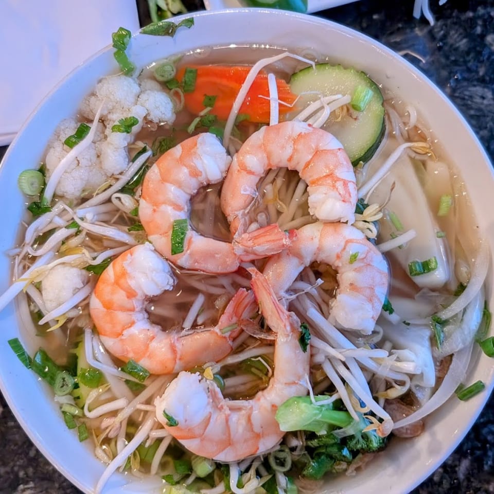 Close-up of a bowl of Vietnamese pho with shrimp, bean sprouts, and vegetables.