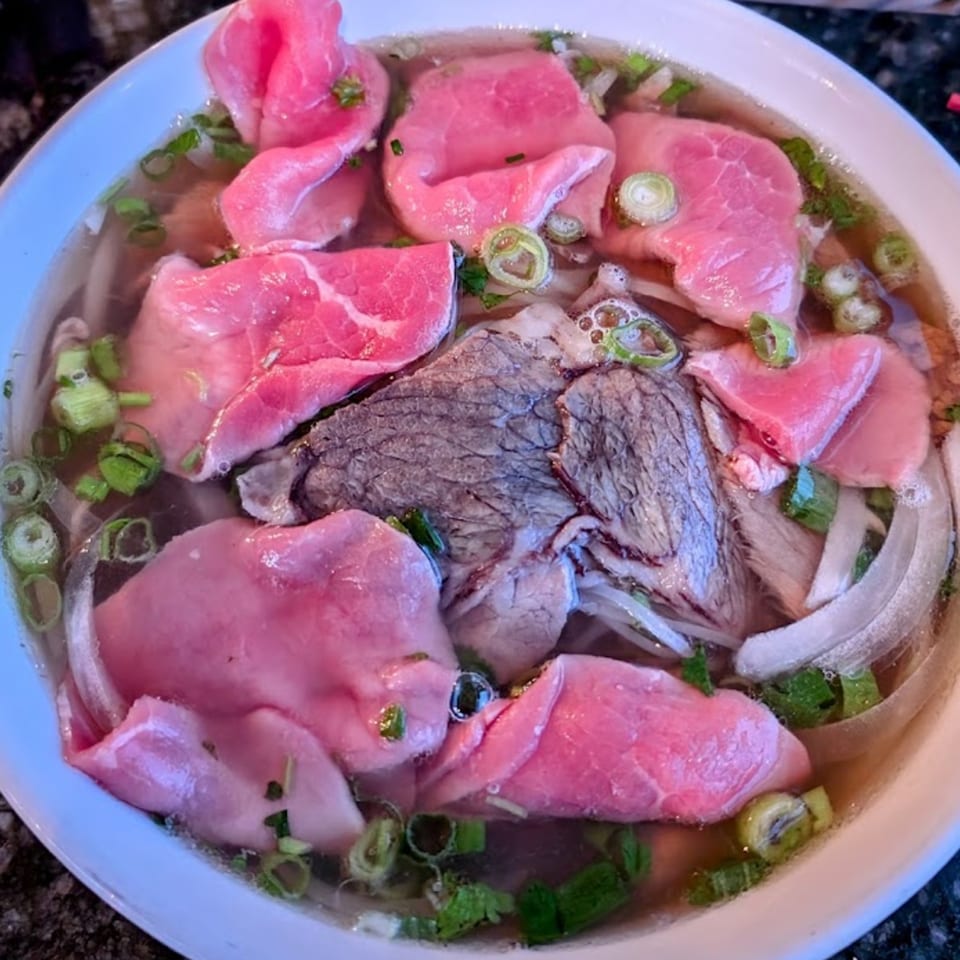 Close-up of a bowl of Vietnamese pho with rare beef slices, cooked beef, onions, and green onions.
